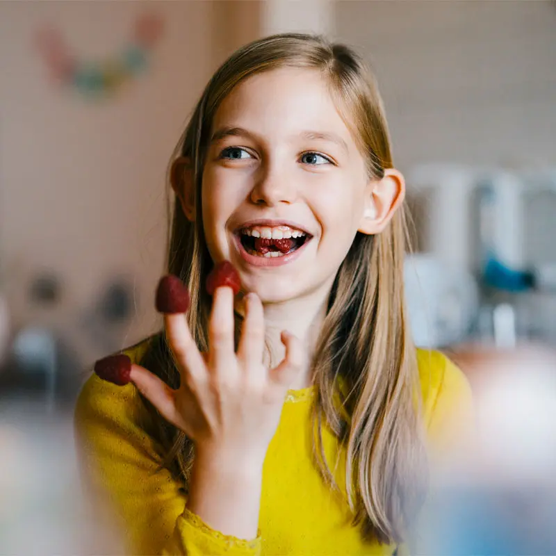 Girl smiling with raspberries on tips of fingers